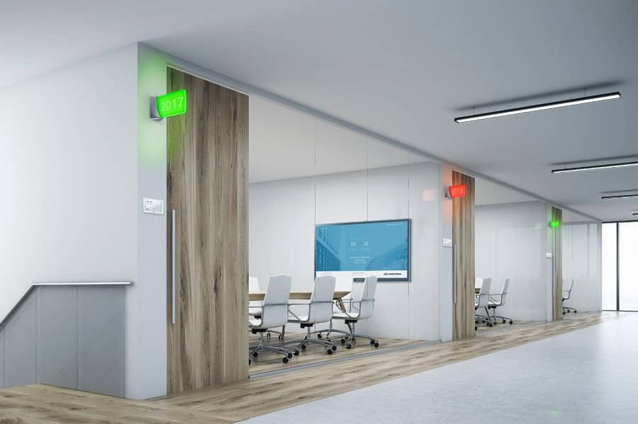 Row of glass-walled meeting spaces with room scheduling occupancy lights illuminated red and green.