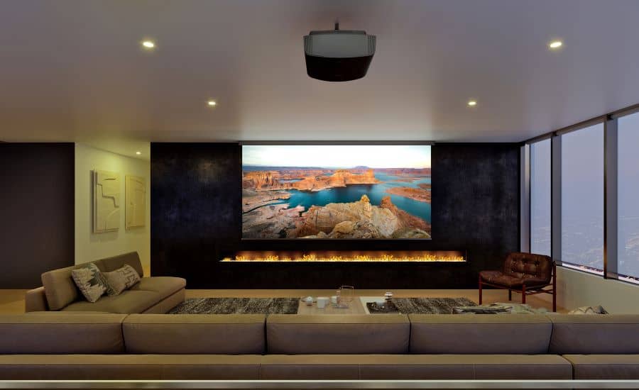 A media room with a sectional, Sony projector, and a movie screen above a lit fire feature.