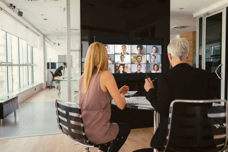 A huddle space with two people video conferencing with numerous remote participants.