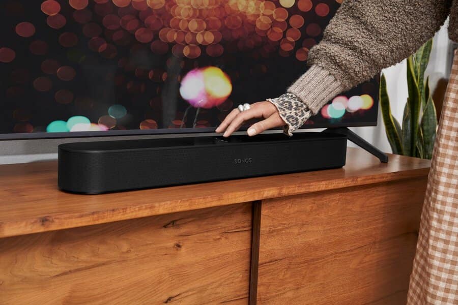 A Sonos soundbar on a TV cabinet with a woman’s hand resting on top of it.