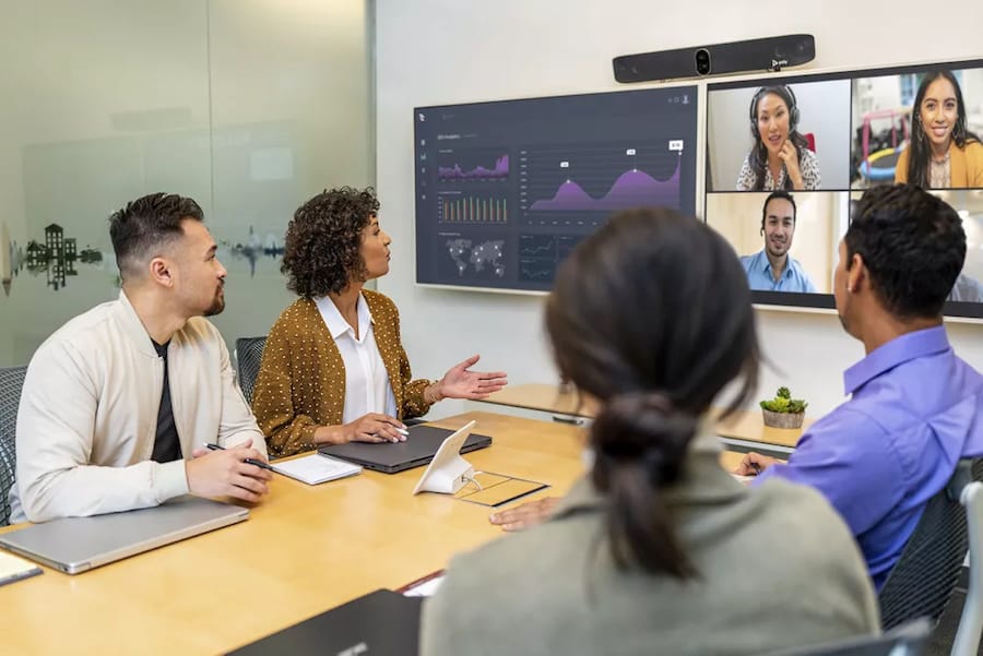 Professionals in Denver use Zoom conferencing for a hybrid meeting, with participants on a screen.